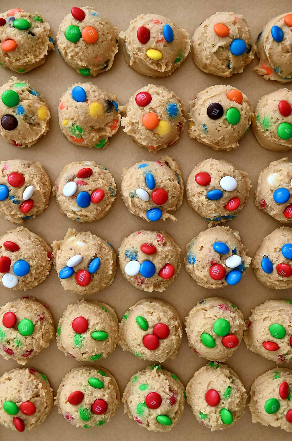 Scooped cookie dough studded with colorful M&Ms on a cookie sheet lined with parchment paper.