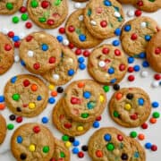 A top-down view of M&M cookies studded with a mix of M&M colors, including red and green, red white and blue, and rainbow.