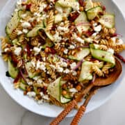 A top-down view of homemade zucchini pasta salad with feta cheese, sun-dried tomatoes, chickpeas and pistachios in a large white bowl.