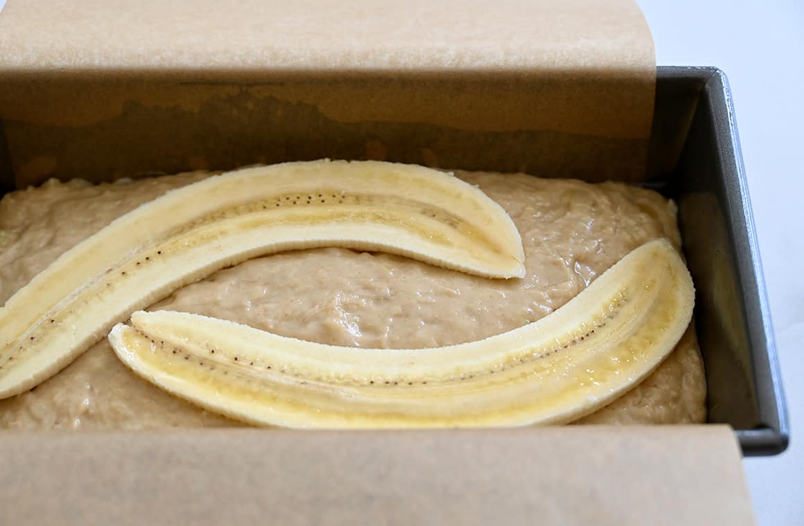 A close-up view of unbaked banana bread topped with banana slices in a loaf pan