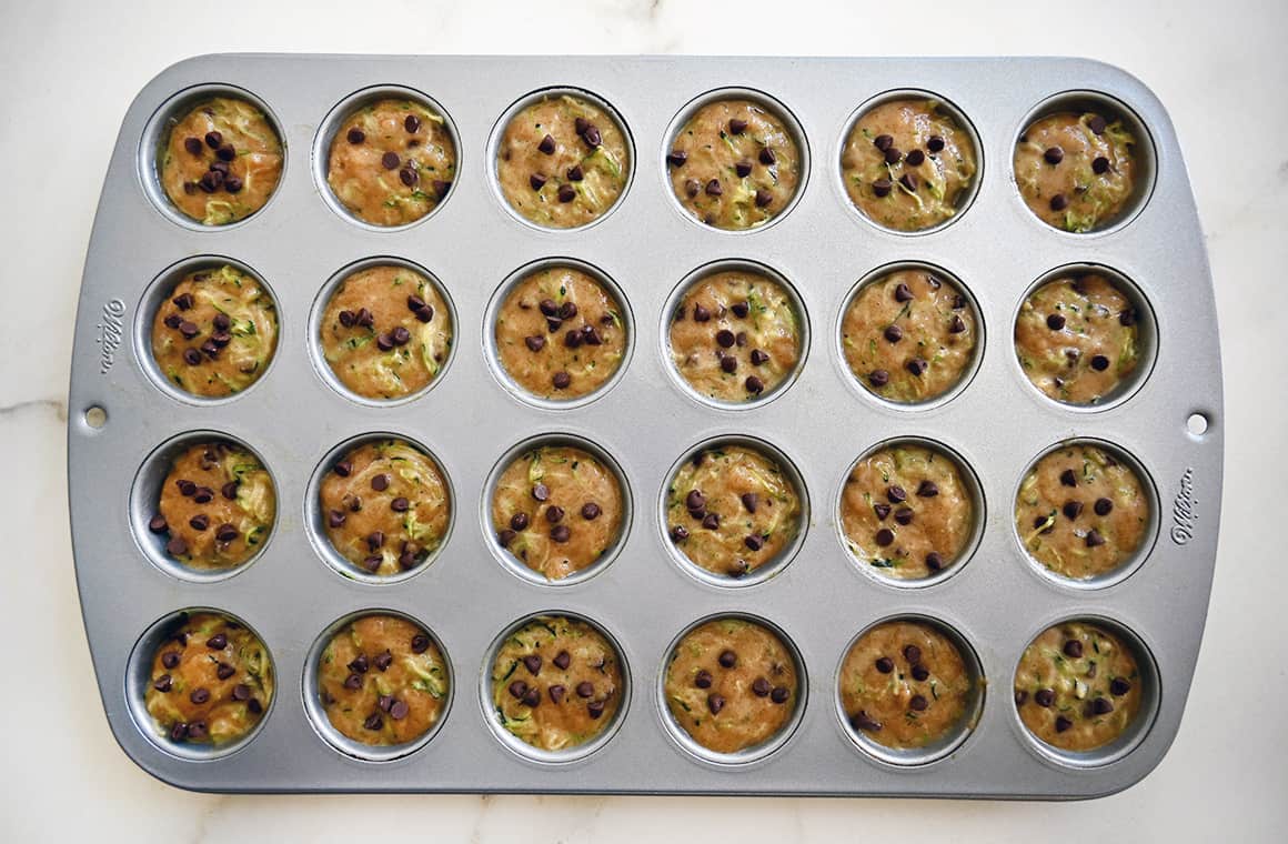 A top-down view of a mini muffin pan filled with batter studded with mini chocolate chips