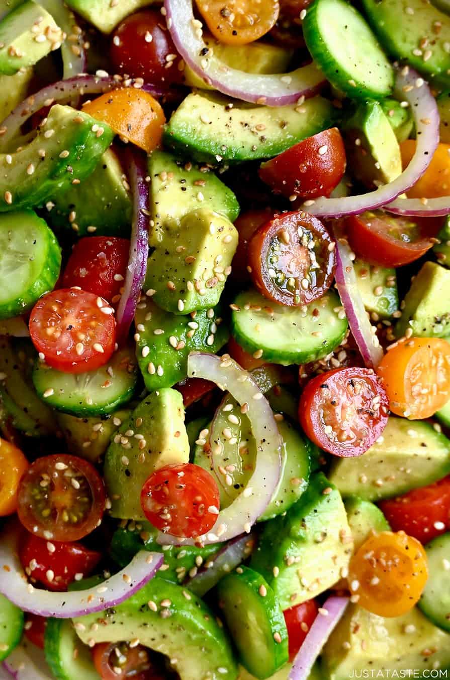 A close up view of diced avocado, red onion, cherry tomatoes and cucumbers topped with sesame seeds