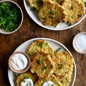 A top-down view of Baked Corn and Zucchini Fritters on a plate next to a small bowl containing sour cream