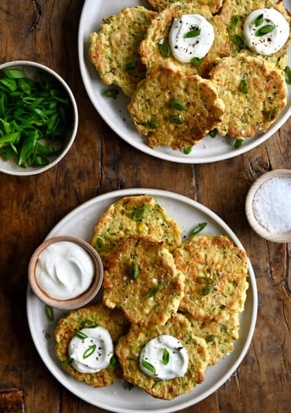 A top-down view of Baked Corn and Zucchini Fritters on a plate next to a small bowl containing sour cream