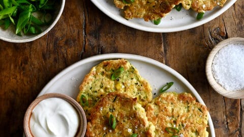 A top-down view of Baked Corn and Zucchini Fritters on a plate next to a small bowl containing sour cream