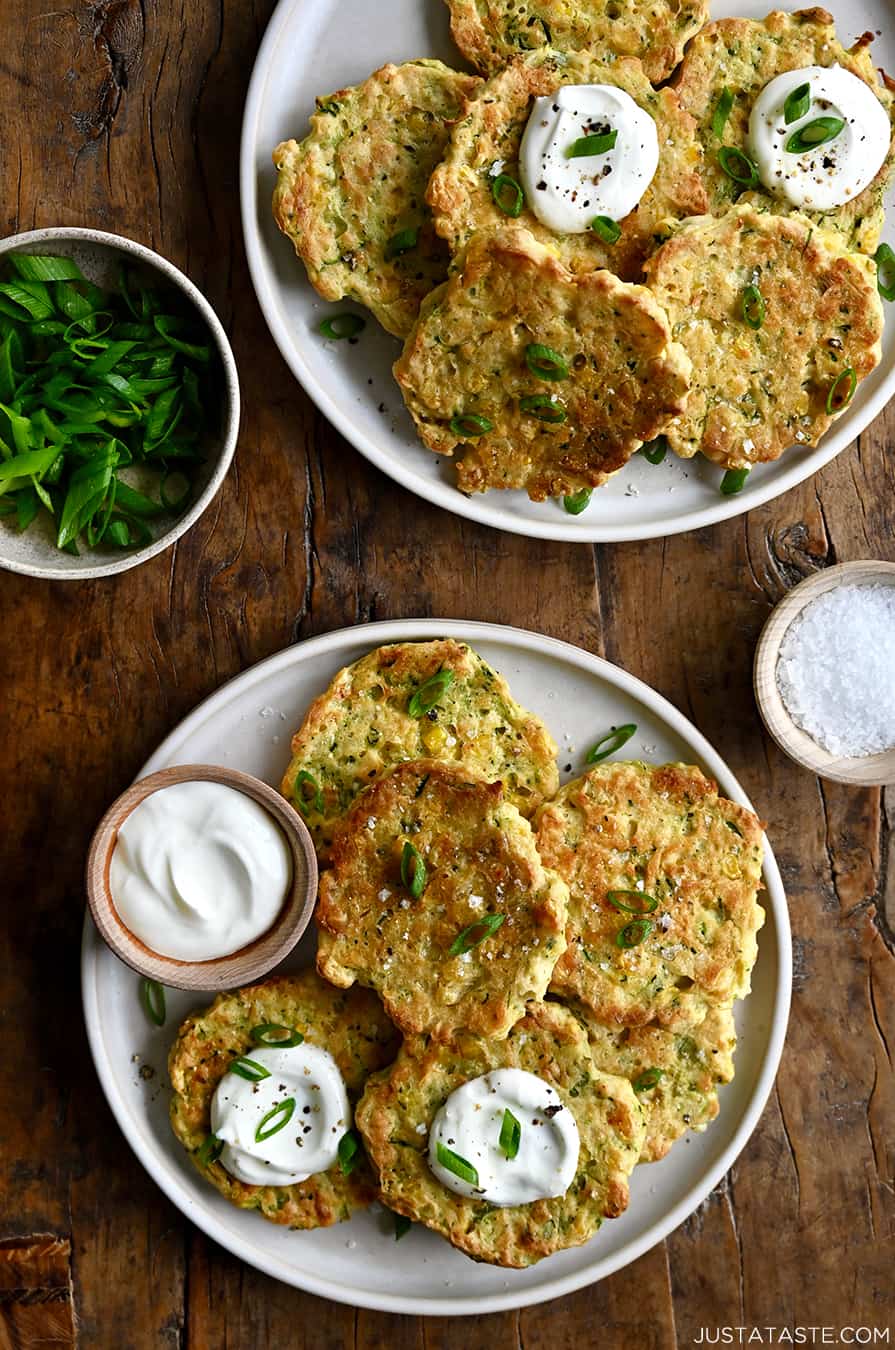 A top-down view of Baked Corn and Zucchini Fritters on a plate next to a small bowl containing sour cream