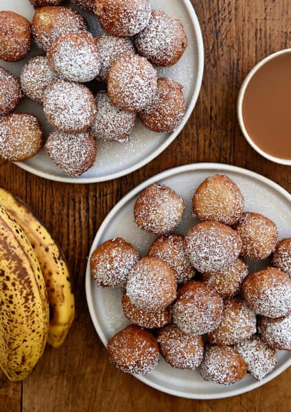 A top-down view of two plates piled high with banana fritters dusted with powdered sugar