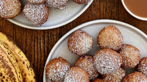A top-down view of two plates piled high with banana fritters dusted with powdered sugar