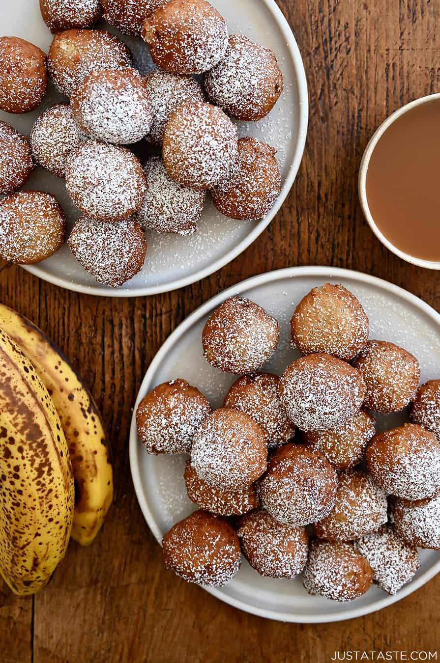 A top-down view of two plates piled high with banana fritters dusted with powdered sugar