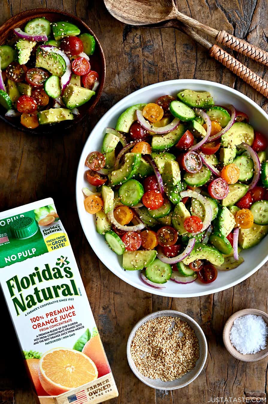 A top-down view of the best avocado and tomato salad with sliced red onions in a white bowl next to a carton of Florida's Natural orange juice