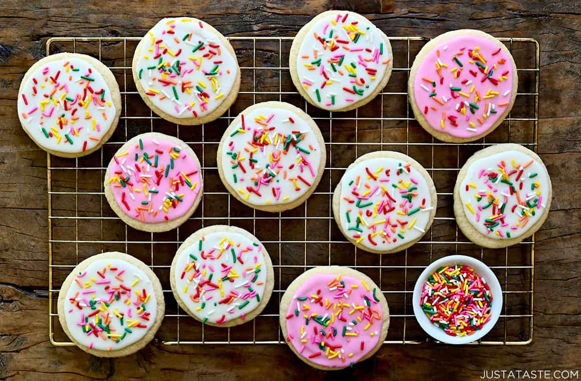 Bakery-style sugar cookies topped with icing and rainbow sprinkles atop a wire rack