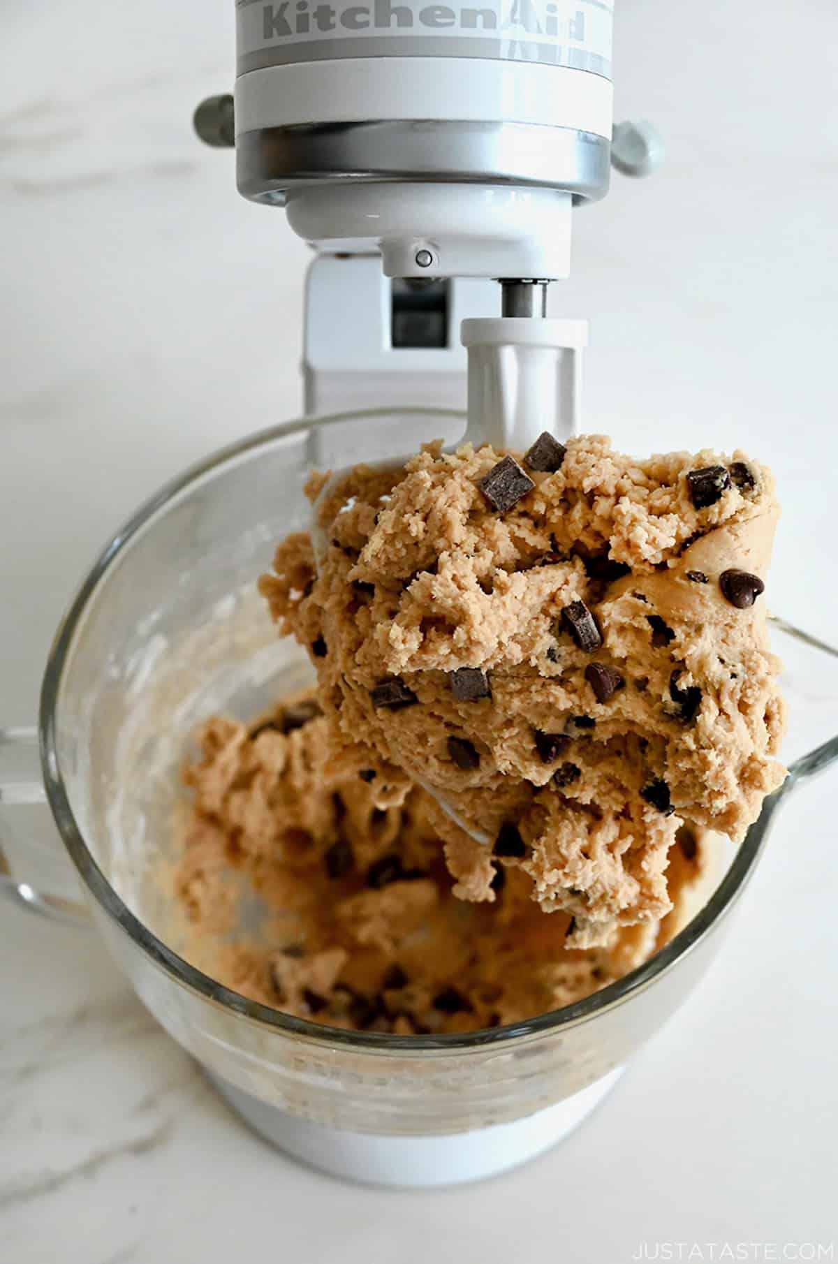 Chocolate chip cookie dough covering the paddle attachment of a stand mixer.