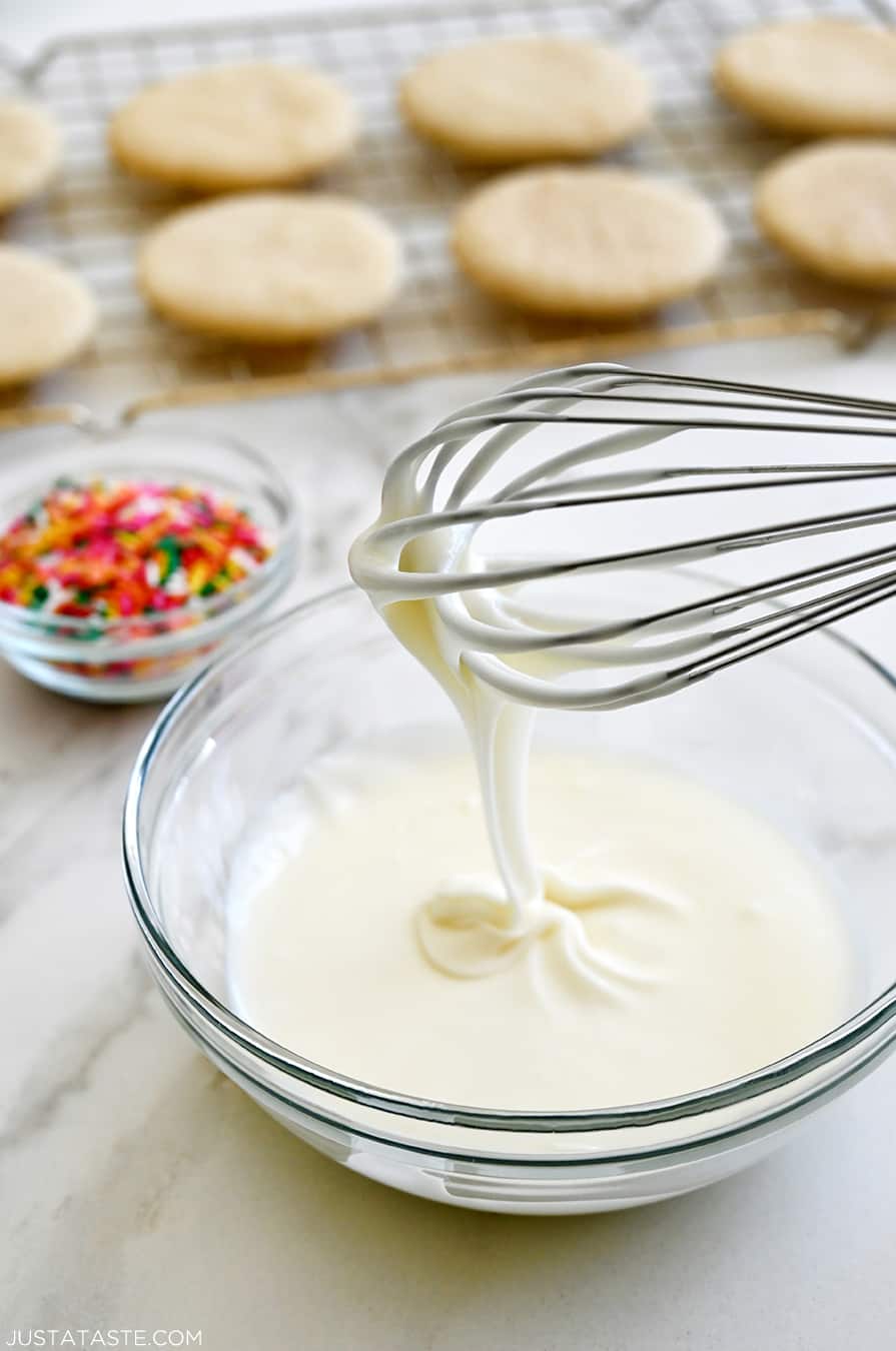 A whisk over a bowl containing frosting made from confectioners' sugar, butter and whole milk