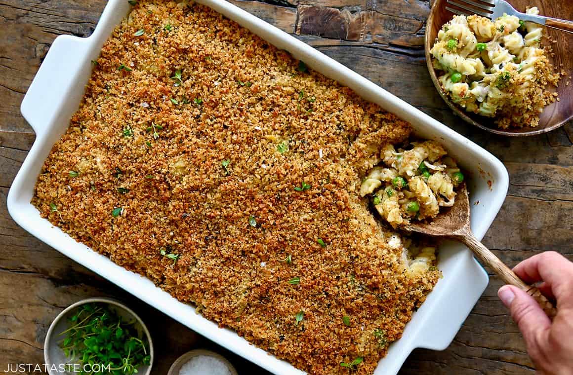 A hand holding a wooden serving spoon in a baking dish containing the best turkey tetrazzini