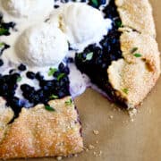 A close-up view of a homemade blueberry galette topped with three scoops of vanilla ice cream and garnished with fresh thyme.