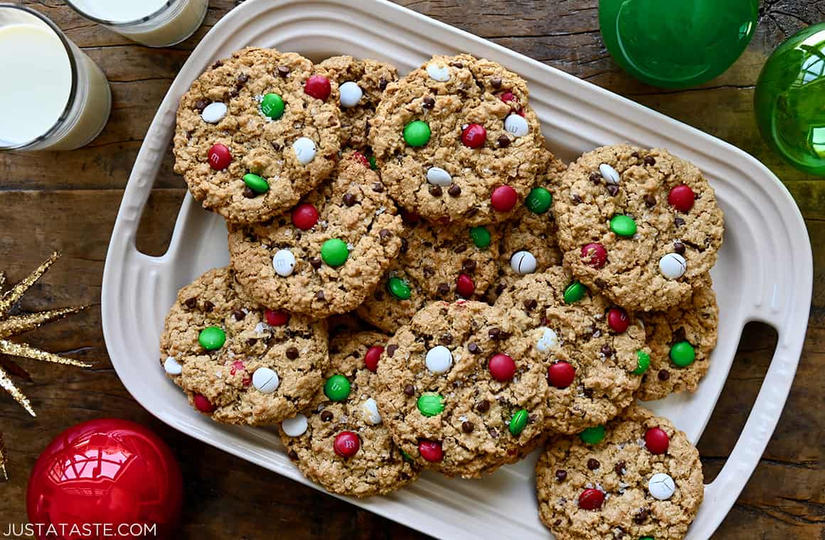 Soft and chewy Christmas Monster Cookies on a platter next to two glasses filled with milk 