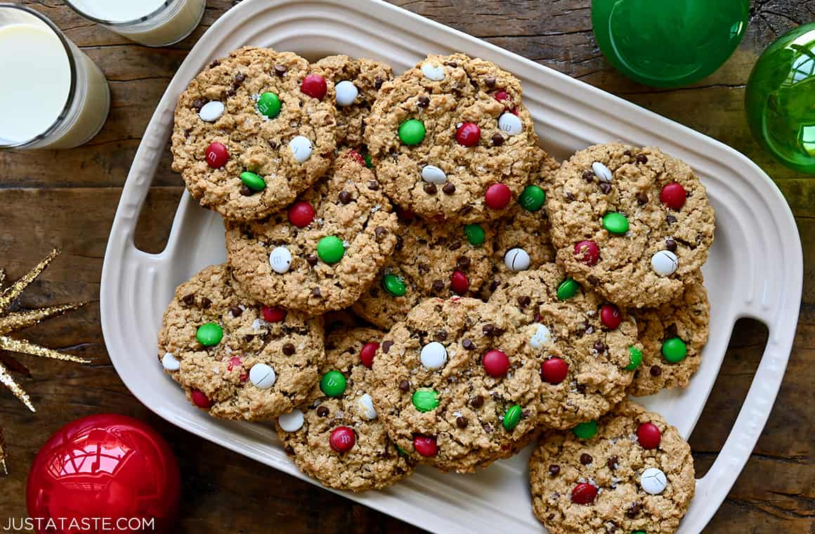 Soft and chewy Christmas Monster Cookies on a platter next to two glasses filled with milk