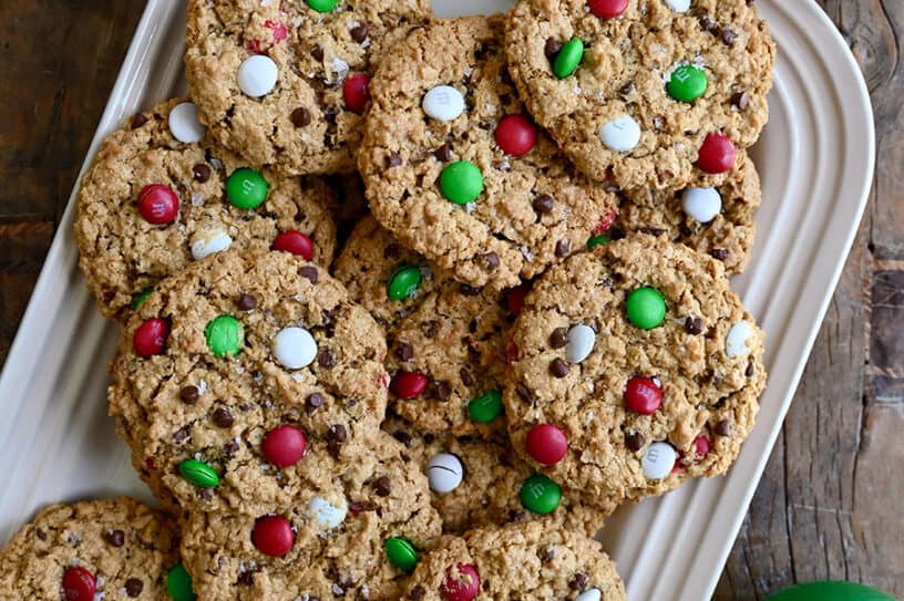 A top-down view of the best Christmas Monster Cookies studded with red, green and white M&Ms on a white serving platter