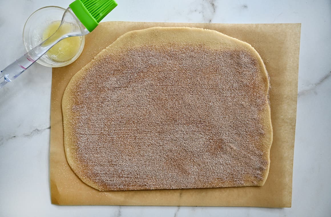 A top-down view of rolled dough on a cutting board next to a small bowl containing melted butter