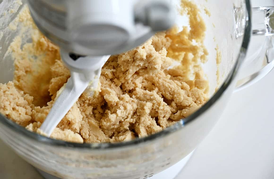A close-up view of cookie dough in a stand mixer bowl with the paddle attachment