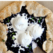 A Blueberry Galette with a small slice missing topped with three scoops of vanilla bean ice cream and fresh thyme.