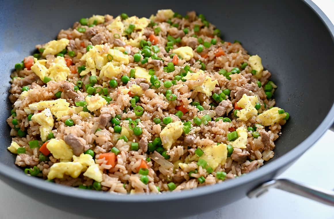 Fried rice with scrambled eggs, pork, peas and carrots in a large wok