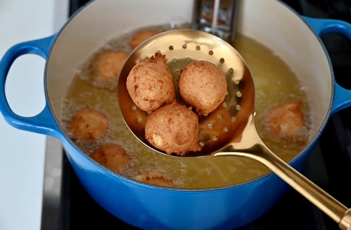 A close-up view of a slotted spoon with three freshly fried fritters 