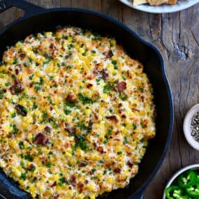 A top-down view of a cast iron skillet containing the best Jalapeño Corn Dip with Bacon next to a bowl filled with tortilla chips