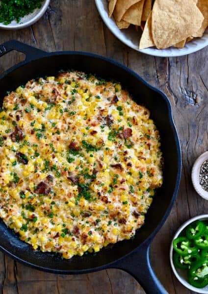 A top-down view of a cast iron skillet containing the best Jalapeño Corn Dip with Bacon next to a bowl filled with tortilla chips