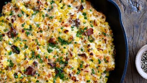 A top-down view of a cast iron skillet containing the best Jalapeño Corn Dip with Bacon next to a bowl filled with tortilla chips