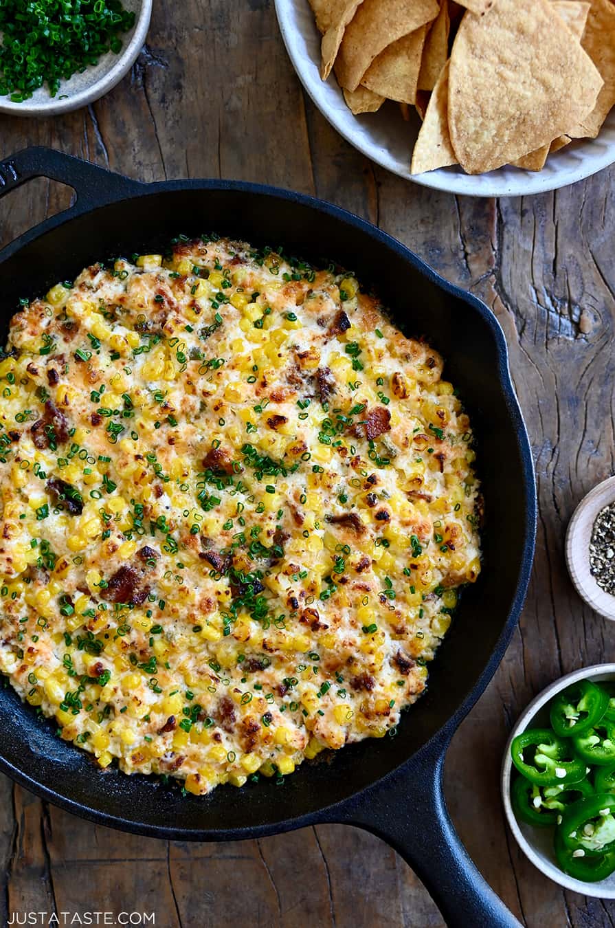 A top-down view of a cast iron skillet containing the best Jalapeño Corn Dip with Bacon next to a bowl filled with tortilla chips