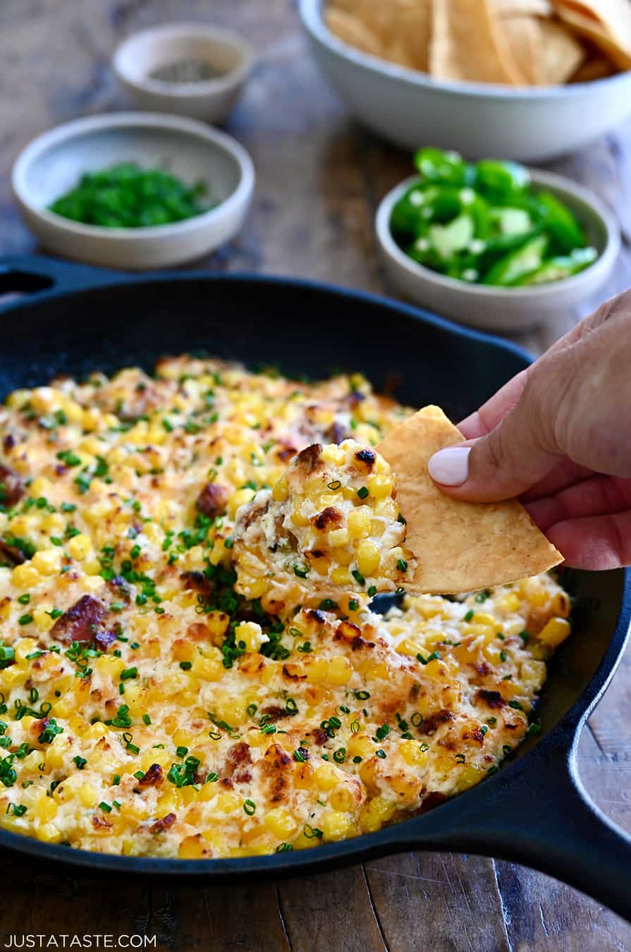 A hand dips a tortilla chip into easy corn dip in a cast iron skillet