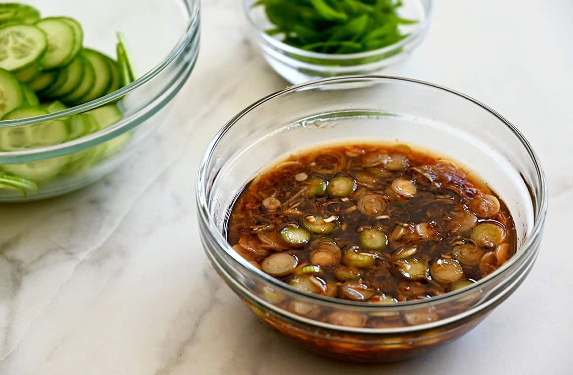 A clear bowl containing soy sauce, minced garlic and ginger, and sliced scallions