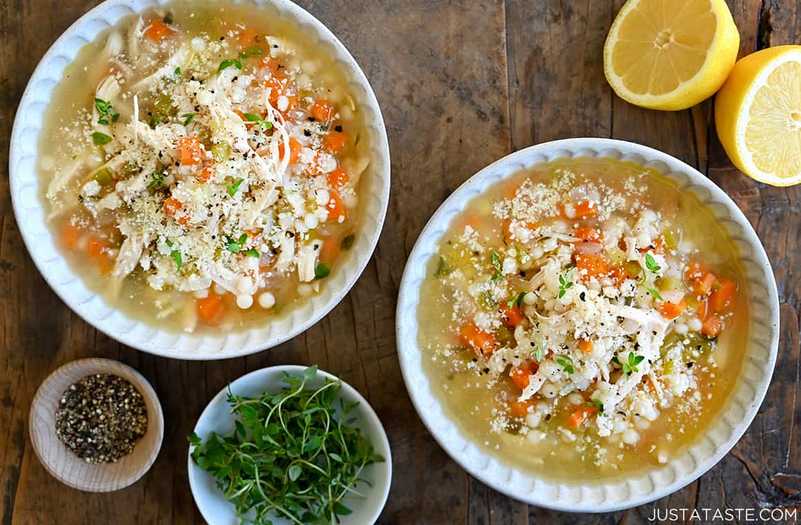 Two white bowls filled with easy leftover turkey soup next to a small bowl containing micro greens, a small bowl containing black pepper and a lemon cut in half 