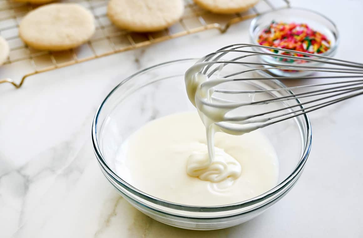 A whisk over a clear bowl containing easy icing made with butter