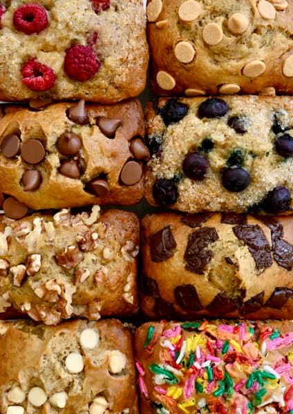 A close-up view of moist mini banana bread loaves all topped with different ingredients, including fresh berries, chocolate chips, walnuts and rainbow sprinkles