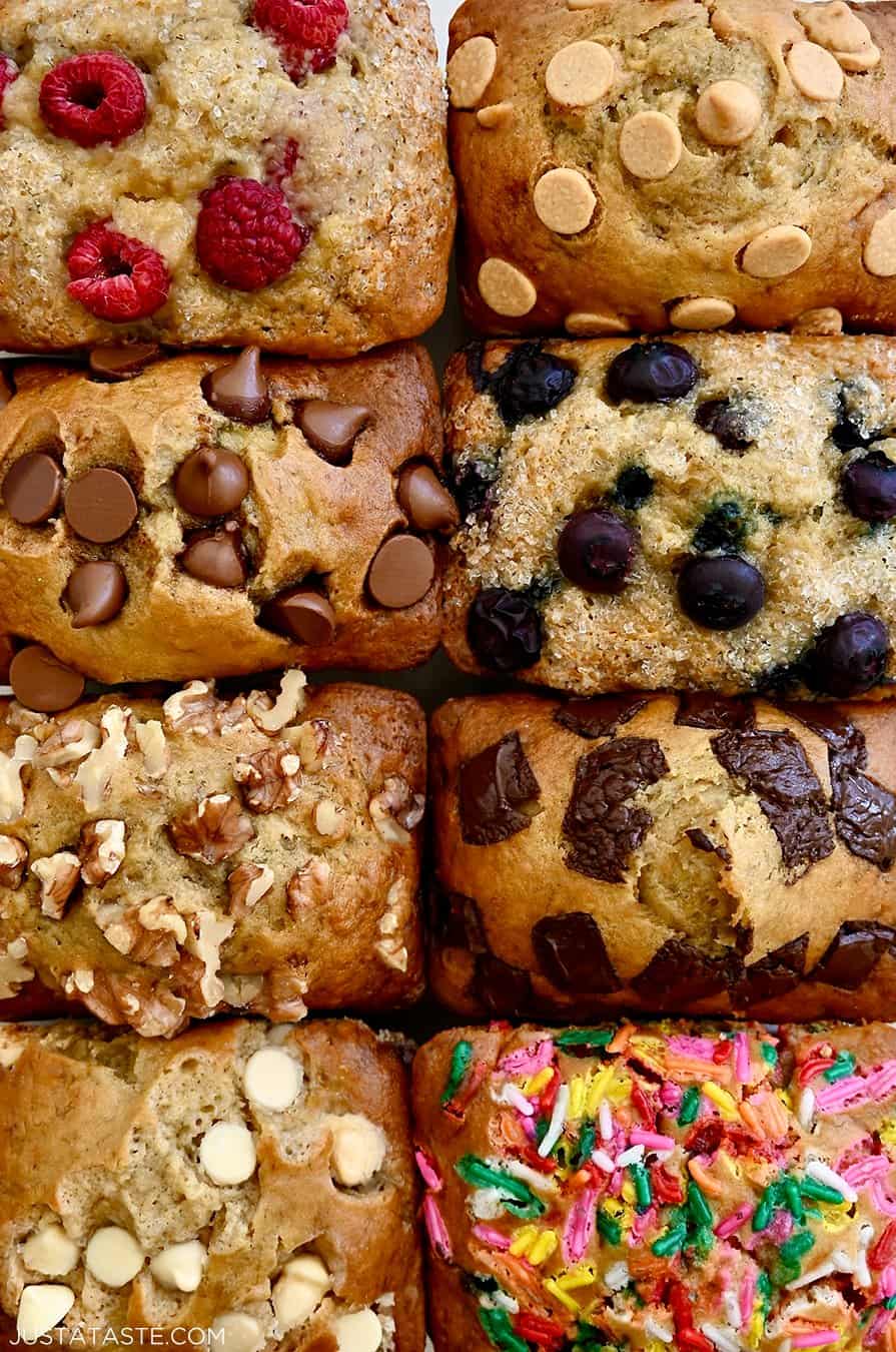 A close-up view of moist mini banana bread loaves all topped with different ingredients, including fresh berries, chocolate chips, walnuts and rainbow sprinkles
