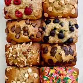 A top-down view of Mini Banana Bread Loaves studded with various mix-ins, including raspberries, chocolate chips, walnuts, sprinkles and more