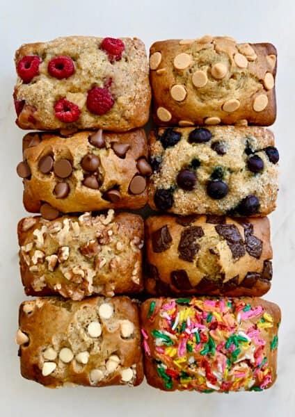 A top-down view of Mini Banana Bread Loaves studded with various mix-ins, including raspberries, chocolate chips, walnuts, sprinkles and more