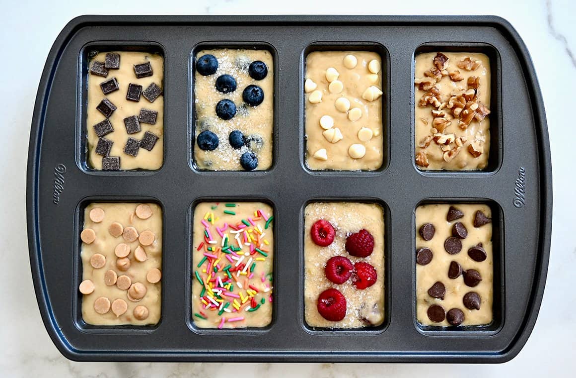 A top-down view of a mini loaf pan containing batter topped with a variety of toppings