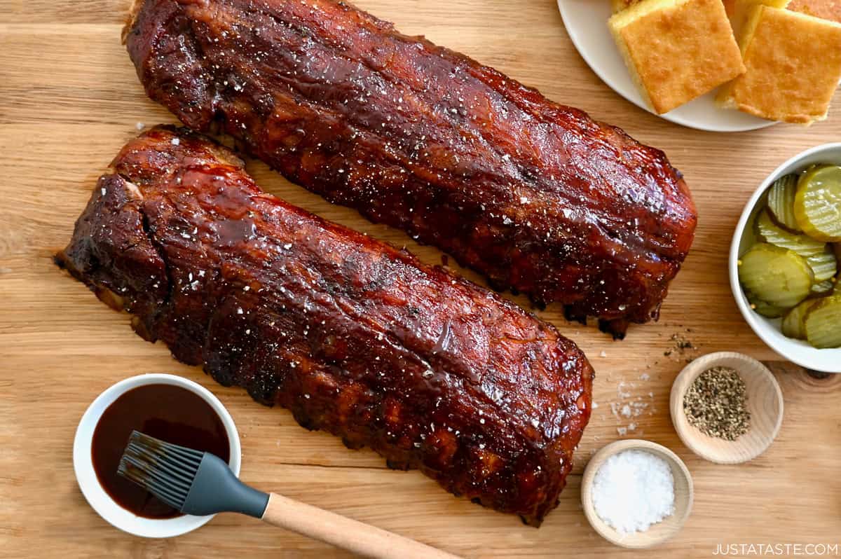 The best Oven-Baked Baby Back Ribs next to a small bowl containing barbecue sauce and a plate piled with cornbread.