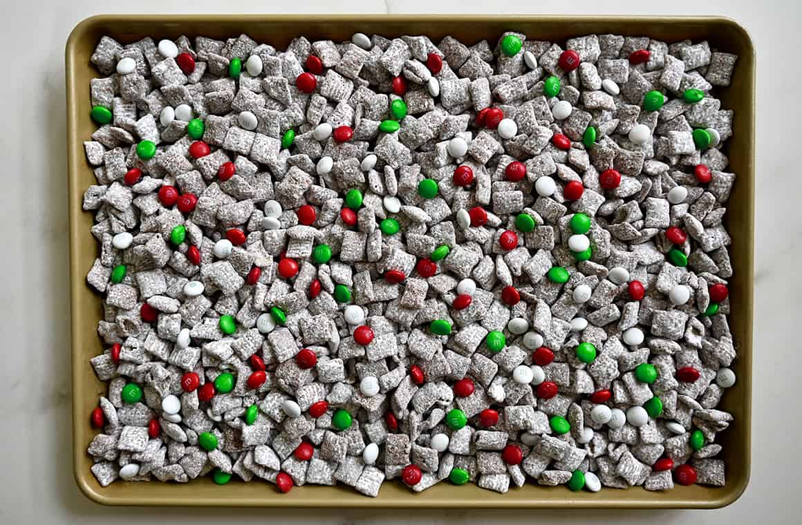 A top-down view of a baking sheet topped with holiday muddy buddies with white, red and green M&Ms