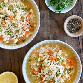 A top-down view of two bowls filled with the best leftover turkey soup next to a lemon cut in half and a small bowl containing micro greens