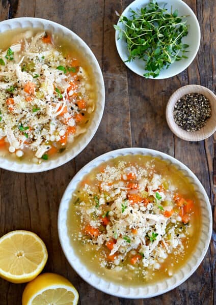 A top-down view of two bowls filled with the best leftover turkey soup next to a lemon cut in half and a small bowl containing micro greens