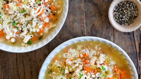 A top-down view of two bowls filled with the best leftover turkey soup next to a lemon cut in half and a small bowl containing micro greens