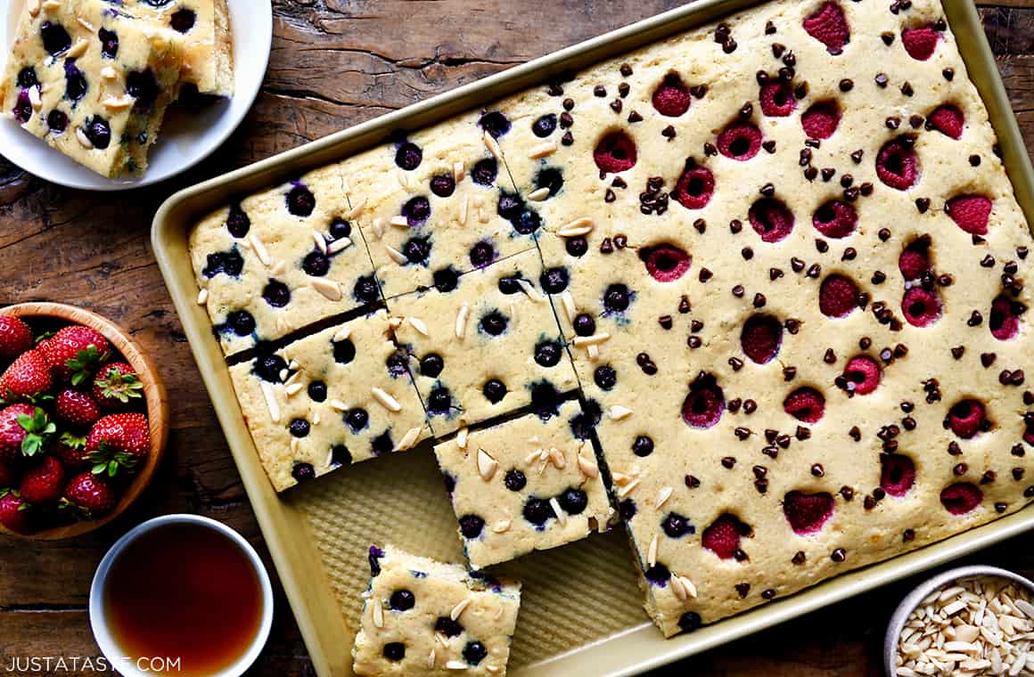 A top-down view of light and fluffy sheet pan pancakes sliced into perfect squares and topped with fresh berries, mini chocolate chips and peanuts