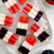 Red, white and blue popsicles on ice next to small bowls containing fresh strawberries and fresh blueberries.