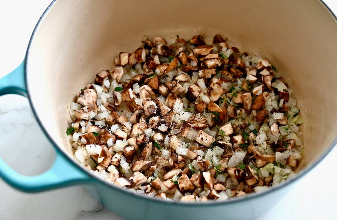 Una grande pentola contenente funghi saltati, cipolle ed erbe aromatiche