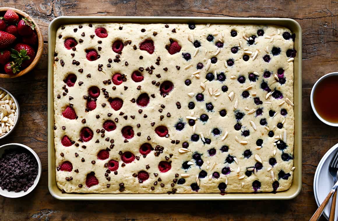 A top-down view of an uncut sheet pan pancake topped with fresh fruit, mini chocolate chips and peanuts