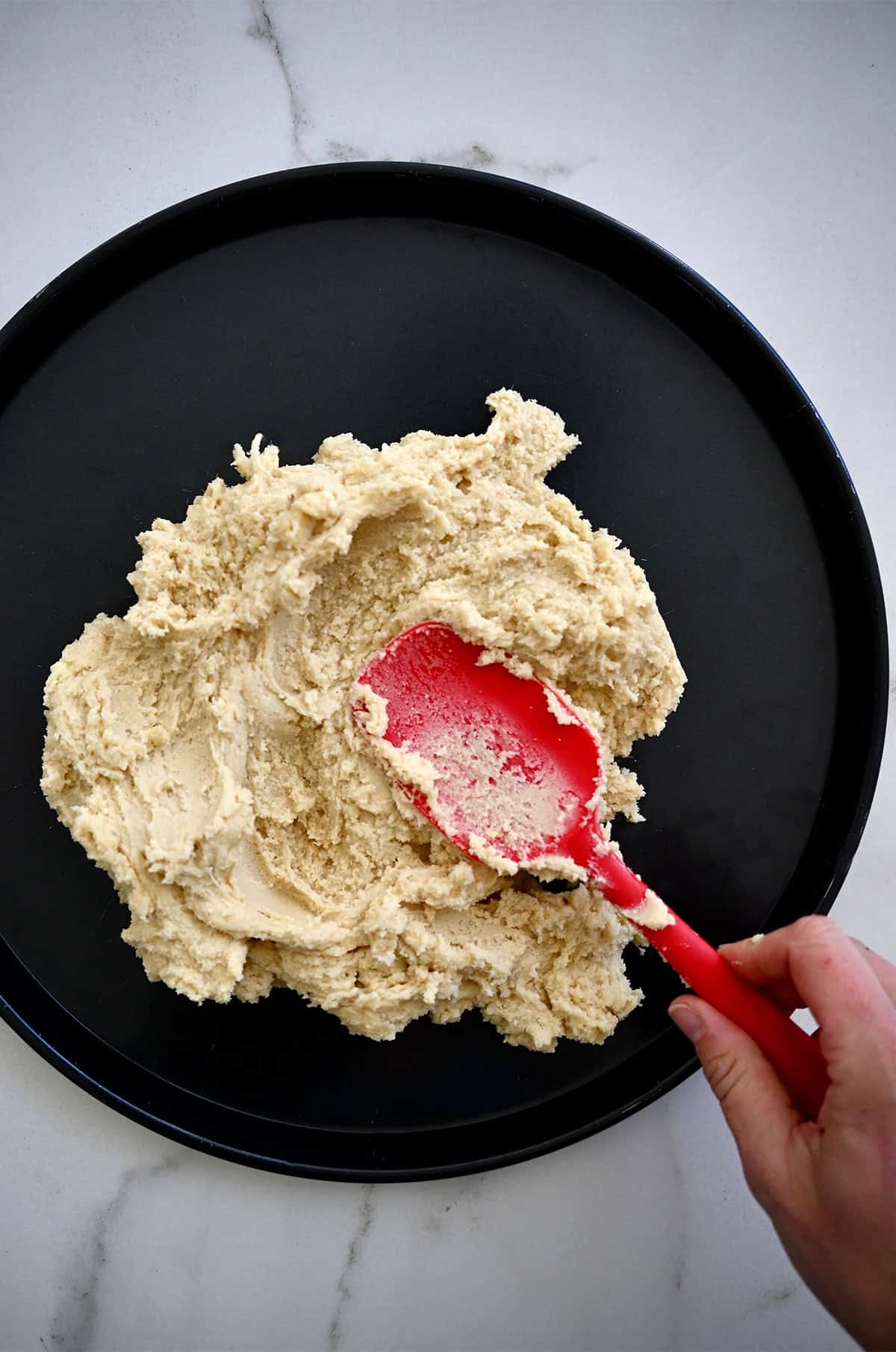 Spreading sugar cookie dough onto a pizza pan with a red spatula.